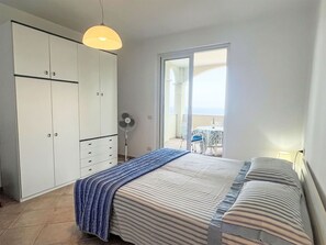 A bedroom with a bed, a wardrobe, a fan, and a view of a balcony with outdoor furniture.