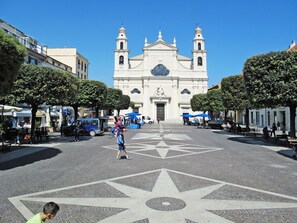 A plaza with a large, ornate building in the background, surrounded by trees and outdoor seating areas.