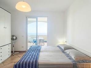 A bedroom with a bed, a fan, a wardrobe, and a view of the outdoors.