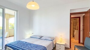 A bedroom with a bed, bedside tables, a lamp, a chair, and a view of a balcony and a laundry area. - Cosy apartment for 5 guests with WIFI, TV, terrace and pets allowed (Pietra Ligure)
