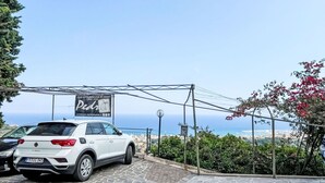 A white car parked in a driveway with a stone-paved area, a signboard, and a view of the sea in the background. - Cosy apartment for 5 guests with WIFI, TV, terrace and pets allowed (Pietra Ligure)