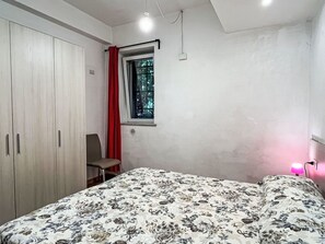 A bedroom with a bed, a wardrobe, a window with a curtain, and a bedside lamp.