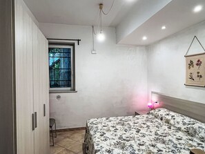 Quarto com cama, janela, luminária na parede e porta.