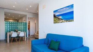 A living room with a blue sofa, a dining table with chairs, and a kitchen area with a green backsplash. - Beautiful apartment for 5 people with A/C, WIFI, TV and patio (Finale Ligure)