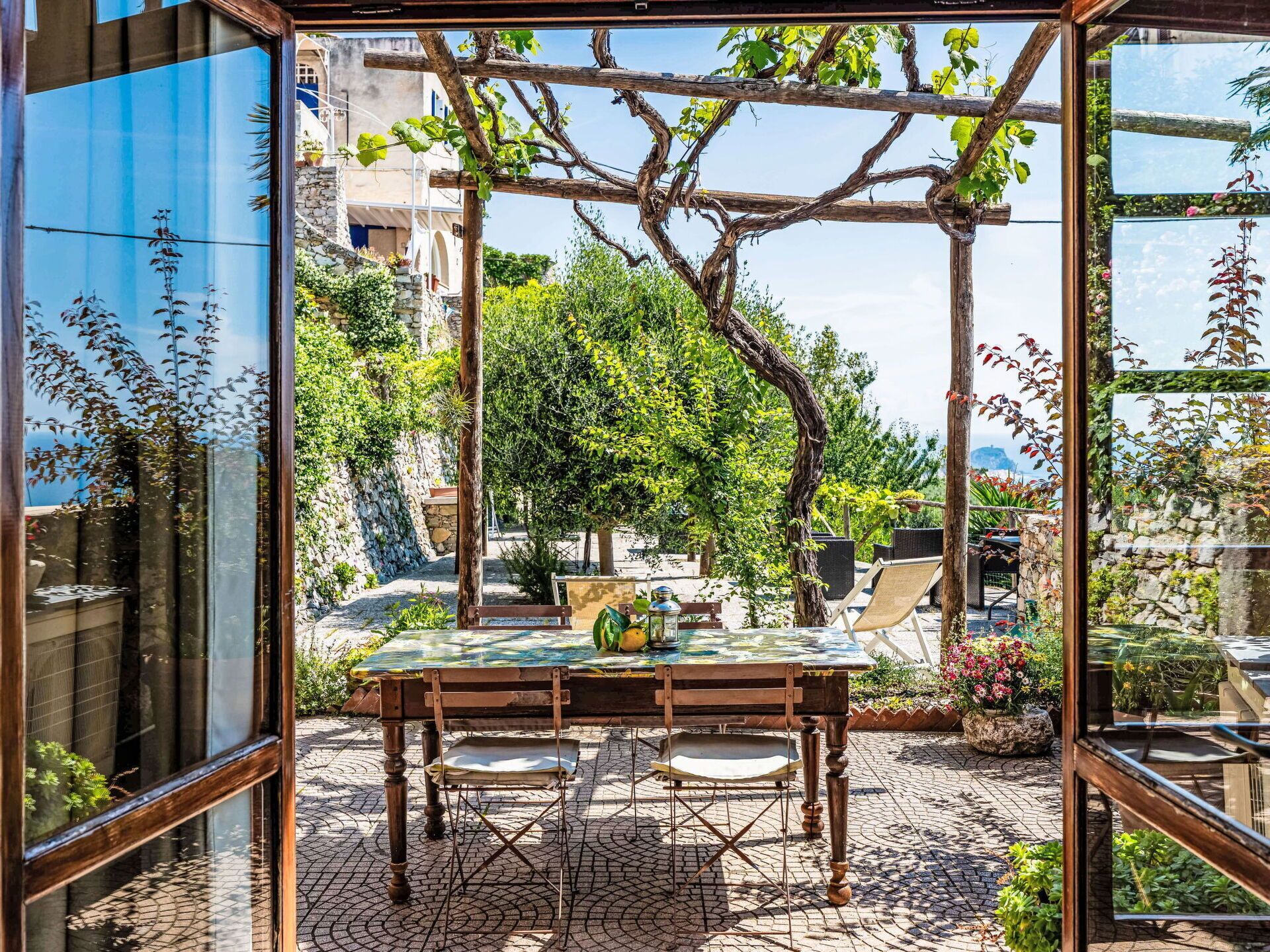Une terrasse avec une table et des chaises, entourée de verdure et agrémentée d’une pergola.