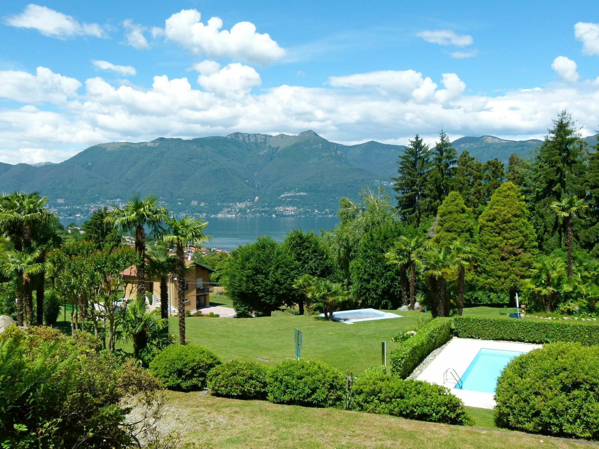 A resort with a swimming pool, lush greenery, and a view of mountains and a lake.