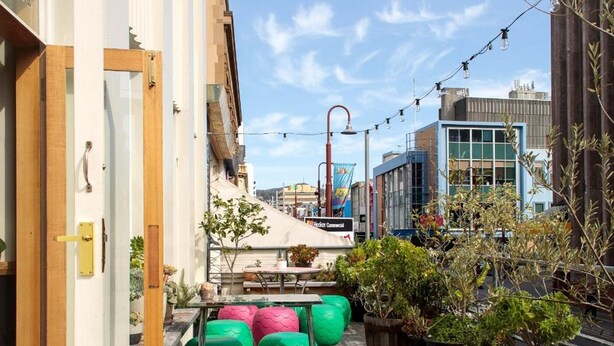 A rooftop terrace with a pink table, green chairs, potted plants, and string lights. - Alabama Hotel Hobart (Hobart)