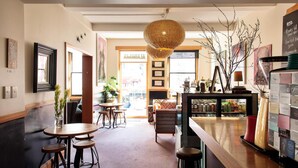 A cozy cafe with wooden tables, a hanging wicker light fixture, and a bar area with stools. - Alabama Hotel Hobart (Hobart)