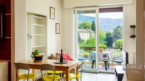 A dining area with a table, chairs, and a view of a building and trees through a glass door. - Lovely apartment for 4 people with WIFI, pool, TV and balcony (Luino)