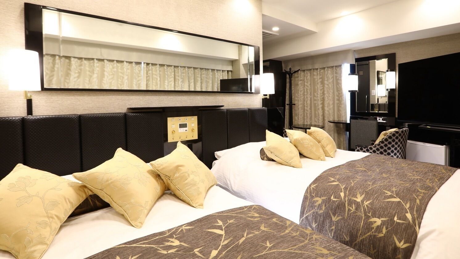 A hotel room with two beds, a large mirror, a flat-screen TV, and a separate seating area with a table and chairs.