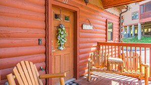 A log cabin with a wooden door marked "122," a porch with wooden chairs, and a welcome mat. - Cozy Cabin 2 - A Great Holiday Family Place - Come Play and Stay! (Branson)