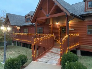 Une cabane en rondins dotée d’un porche décoré de guirlandes lumineuses, d’une clôture en bois et d’un petit sentier menant à l’entrée.