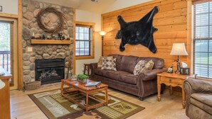 A cozy living room with a stone fireplace, a brown leather sofa, and a mounted animal head on the wall. - Cozy Cabin 2 - A Great Holiday Family Place - Come Play and Stay! (Branson)