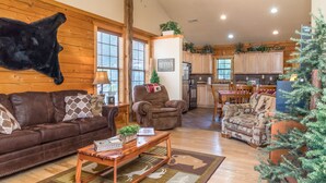 A cozy living room with a brown leather couch, a brown armchair, and a wooden coffee table. There is a small Christmas tree and a mounted animal head on the wall. - Cozy Cabin 2 - A Great Holiday Family Place - Come Play and Stay! (Branson)