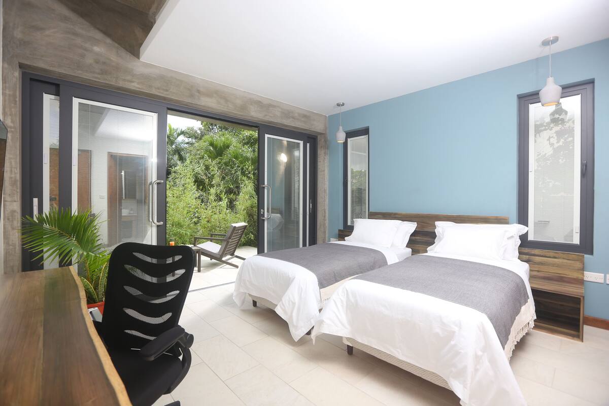 A modern bedroom with two beds, a dining table, and a chair.