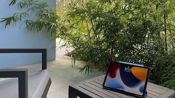Un espacio exterior moderno con asientos, una computadora portátil sobre una mesa, rodeado de plantas de bambú y un muro de piedra.