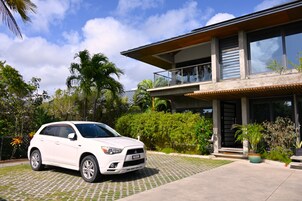 Een modern huis met twee verdiepingen en een witte SUV op de oprit.