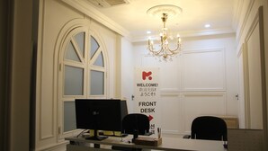 Una recepción con una computadora, dos sillas, una araña de cristal y un cartel de bienvenida.