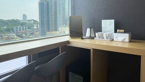 Un escritorio moderno con una computadora portátil, una cafetera y una caja de pañuelos. Una ventana muestra un paisaje urbano con edificios altos.