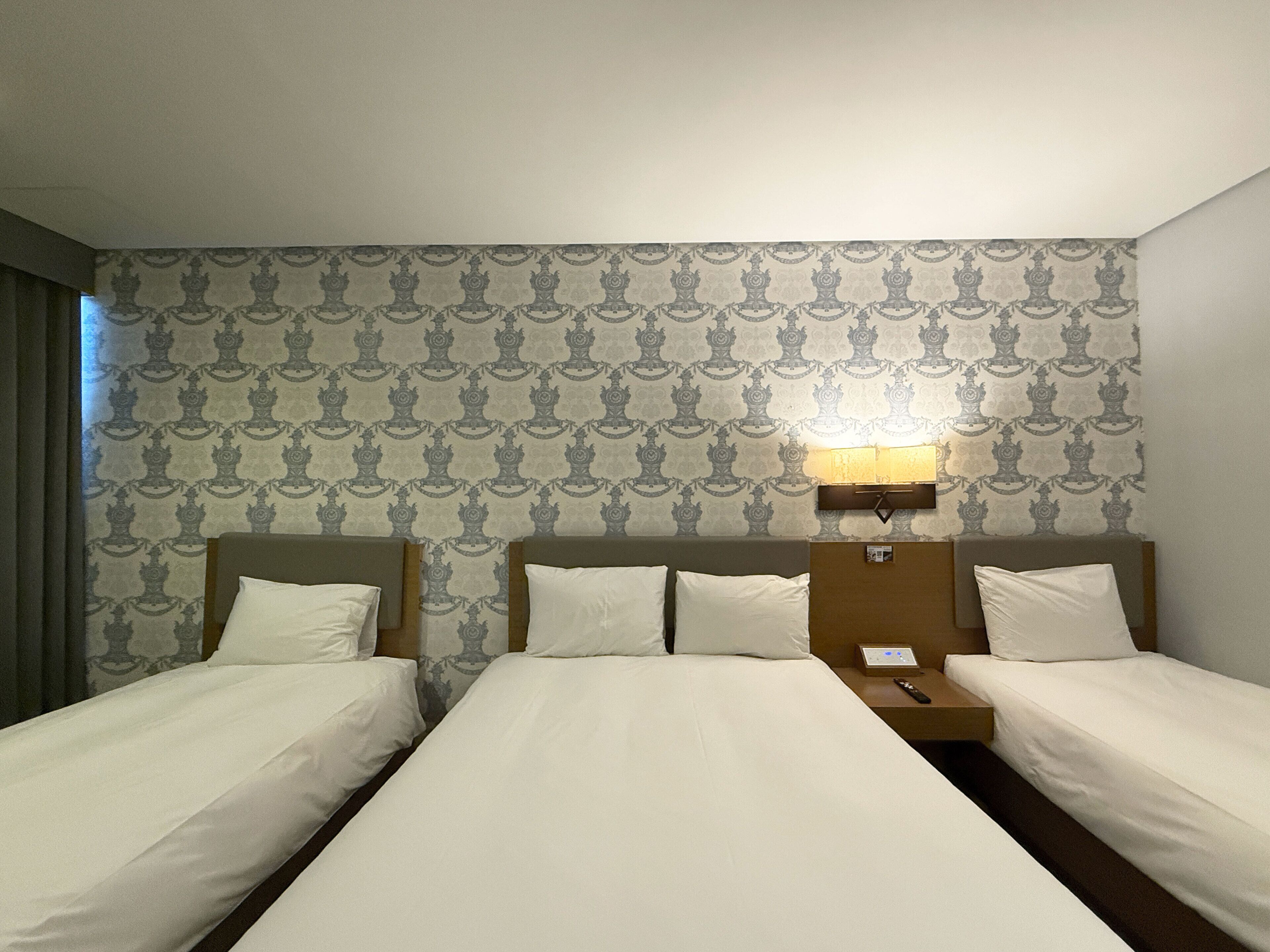 Habitació d'hotel amb dos llits individuals, una tauleta de nit amb una làmpada i un paper pintat amb dibuixos.