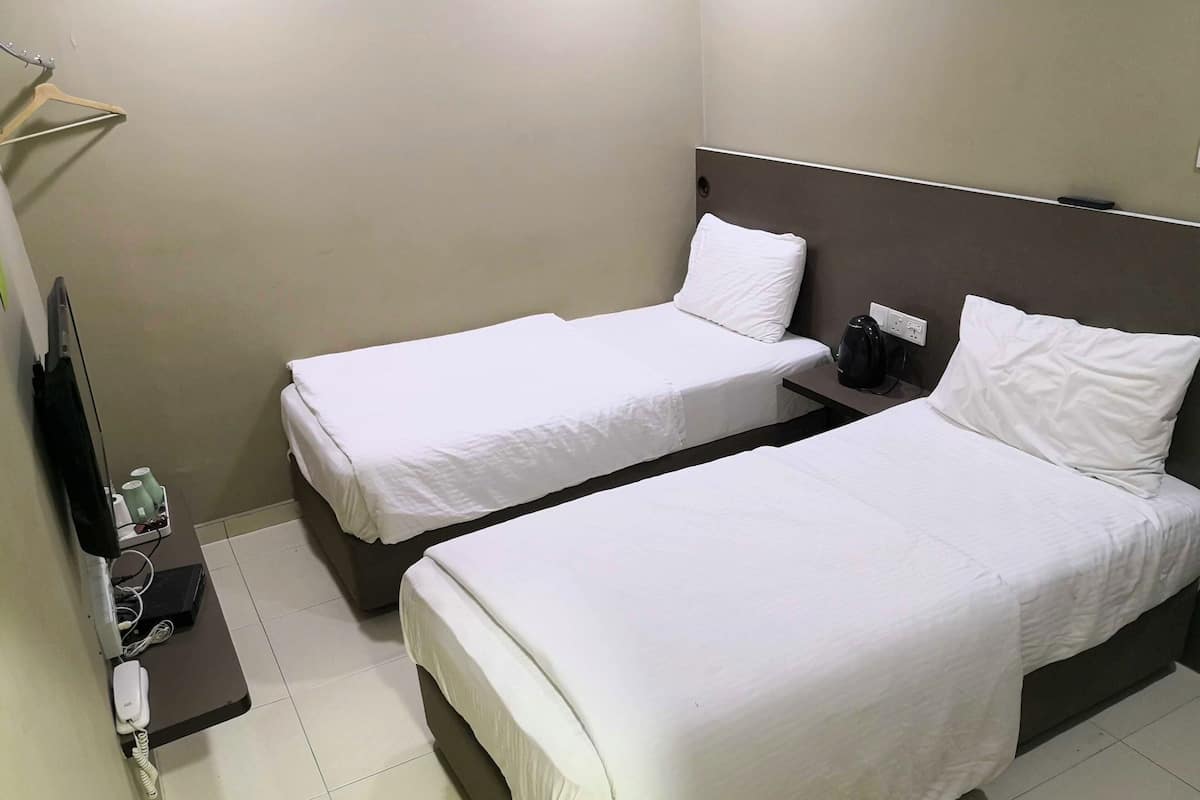 Une chambre d’hôtel avec deux lits simples, une petite table avec un téléphone et une bouilloire, et un téléviseur fixé au mur.