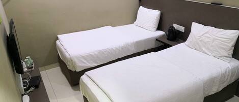 Habitación de hotel con dos camas individuales, una mesita con un teléfono y una tetera, y un televisor instalado en la pared.