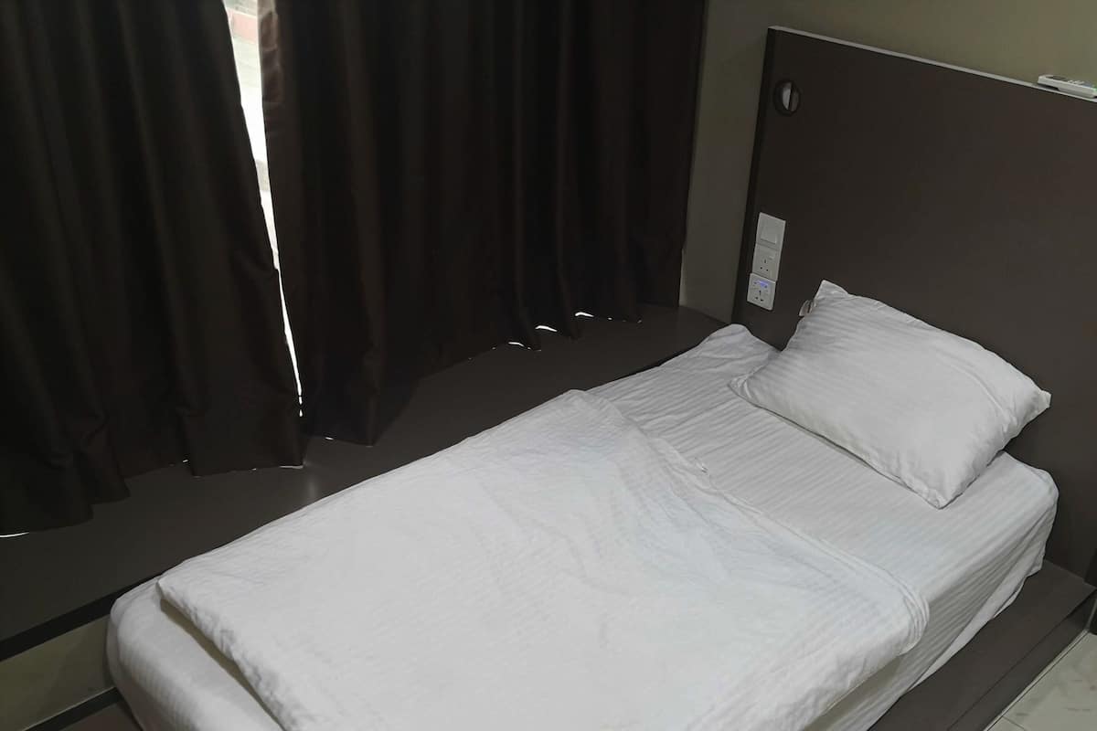 Un lit simple avec une literie blanche, dans une chambre dont la tête de lit est de couleur sombre et où une prise électrique est visible.