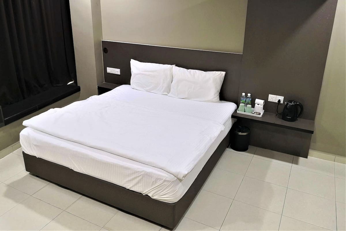 Une chambre d’hôtel moderne avec un grand lit, une tête de lit, une table de chevet avec un téléphone et des bouteilles d’eau, et une poubelle.