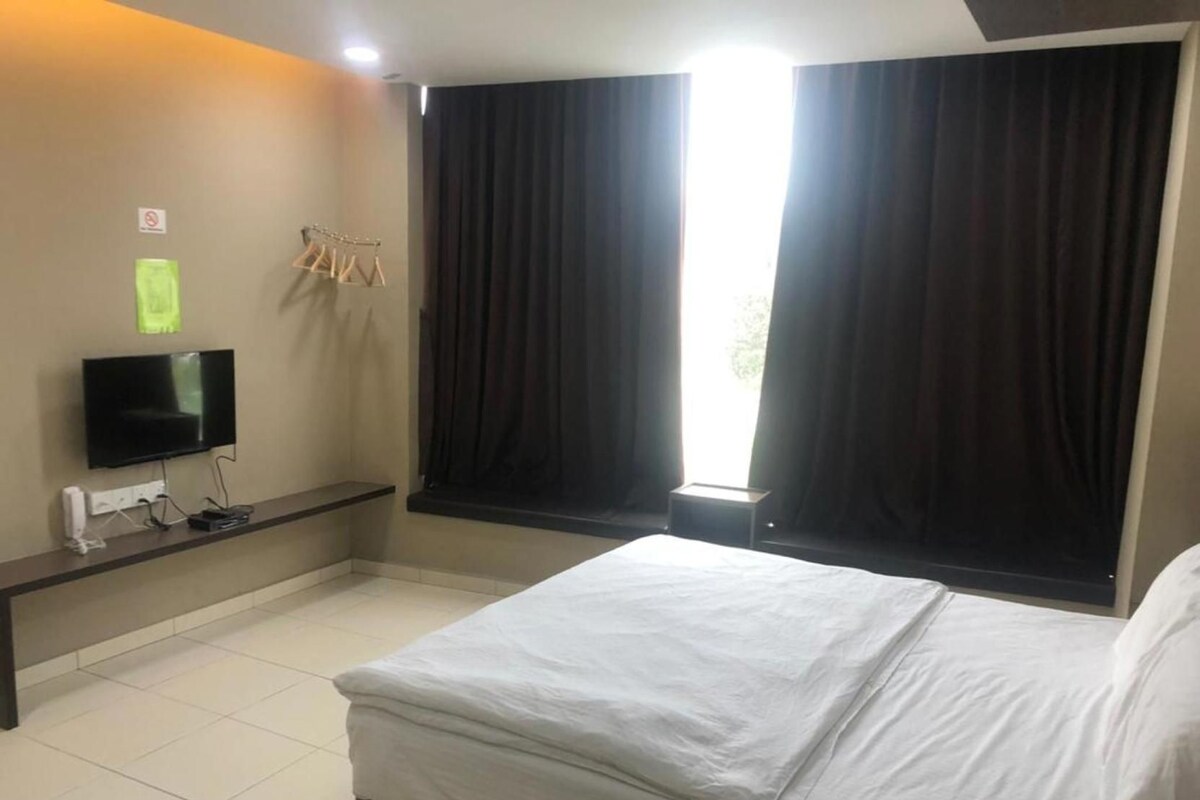 Ein Hotelzimmer mit Bett, Flachbildfernseher, kleinem Tisch und einem Fenster mit Vorhängen.