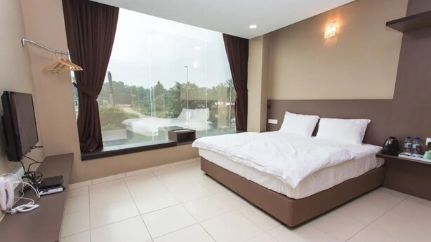 A modern hotel room with a large bed, a desk with a telephone and a laptop, a TV, and a window with curtains. - Tropika Garden Hotel Kulai (Kulai)