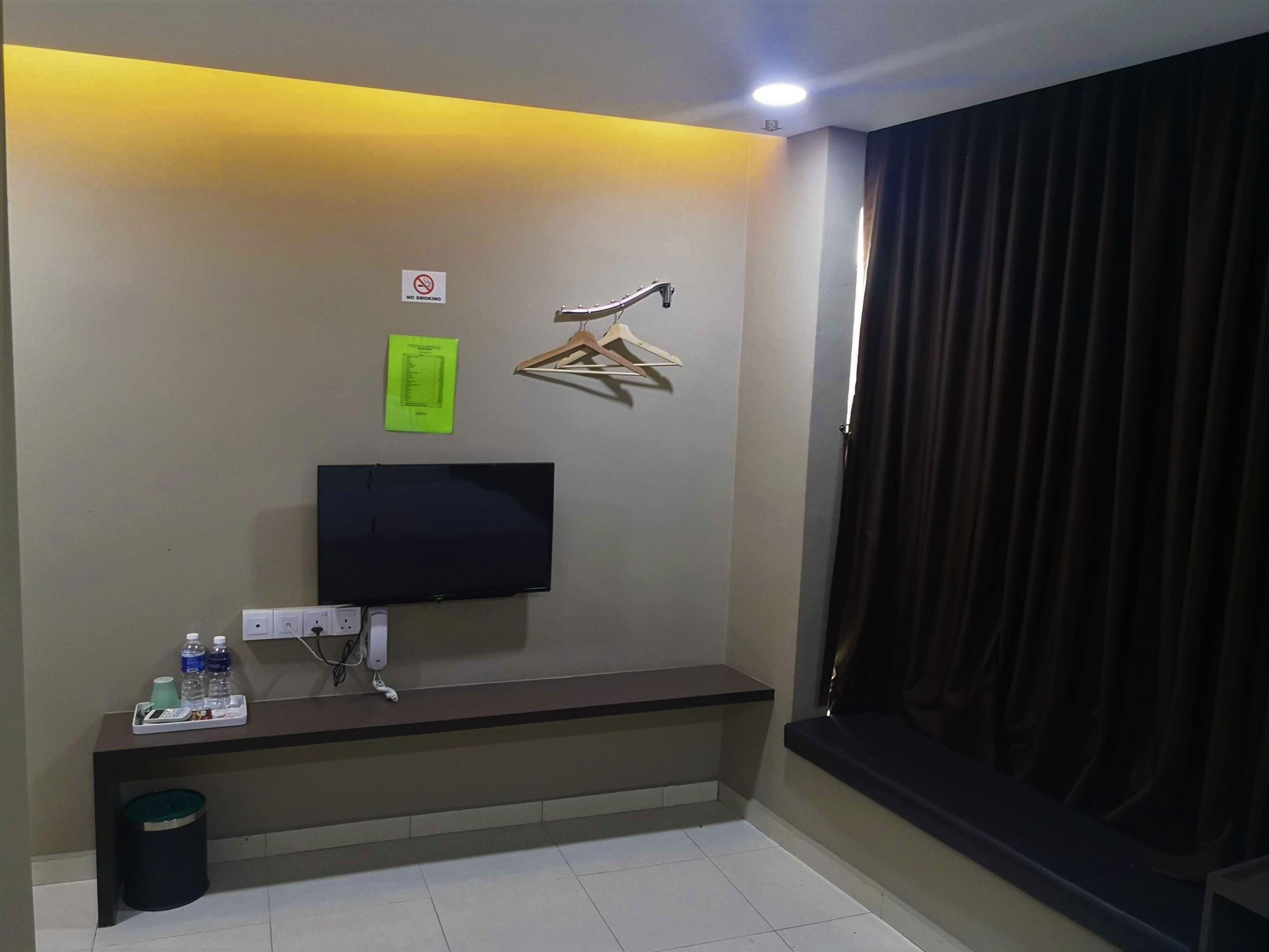 A room with a flat-screen TV mounted on the wall, a bench, a trash bin, and a no-smoking sign.