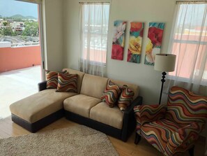 Un salon avec un canapé d’angle beige, des coussins rayés aux couleurs vives, un lampadaire et trois tableaux floraux accrochés au mur.