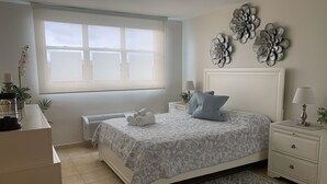 A bedroom with a bed, bedside tables, a radiator, a window, and decorative wall art. - Oasis Luxury Penthouse with Ocean & Marina Views (Fajardo)
