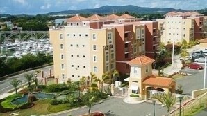 A multi-story hotel with a central courtyard, a swimming pool, and a marina in the background. - Oasis Luxury Penthouse with Ocean & Marina Views (Fajardo)
