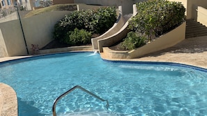 A swimming pool with a metal ladder, surrounded by a tiled deck and a landscaped area with bushes. - Oasis Luxury Penthouse with Ocean & Marina Views (Fajardo)