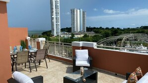 A balcony with outdoor furniture, a dining table, and chairs. There are two tall buildings in the background. - Oasis Luxury Penthouse with Ocean & Marina Views (Fajardo)