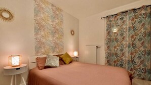 Un dormitorio con una cama grande, una mesita de noche con lámpara, una pared con diseño de hojas y una ventana con cortinas.