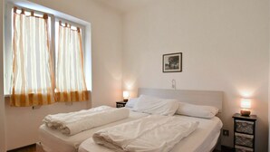 A double bed with white linens, two bedside tables with lamps, a window with curtains, and a framed picture on the wall. - Lovely apartment for 6 people with WIFI, TV, balcony and pets allowed (Crone)