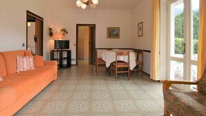 Ein Wohnzimmer mit einer Couch, einem Fernsehtisch, einem Esstisch mit Stühlen und einem großen Fenster mit Vorhängen.