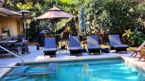 Zona de piscina con sillones de descanso, un espacio de estar cubierto y una piscina.