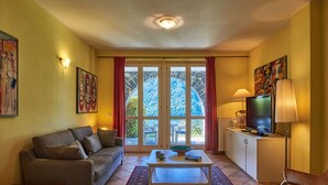 A living room with a sofa, a coffee table, a TV, and a view through a glass door.
