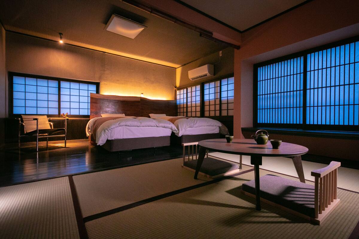 A traditional Japanese-style room with tatami flooring, a low table with a tea set, and a large shoji screen window.