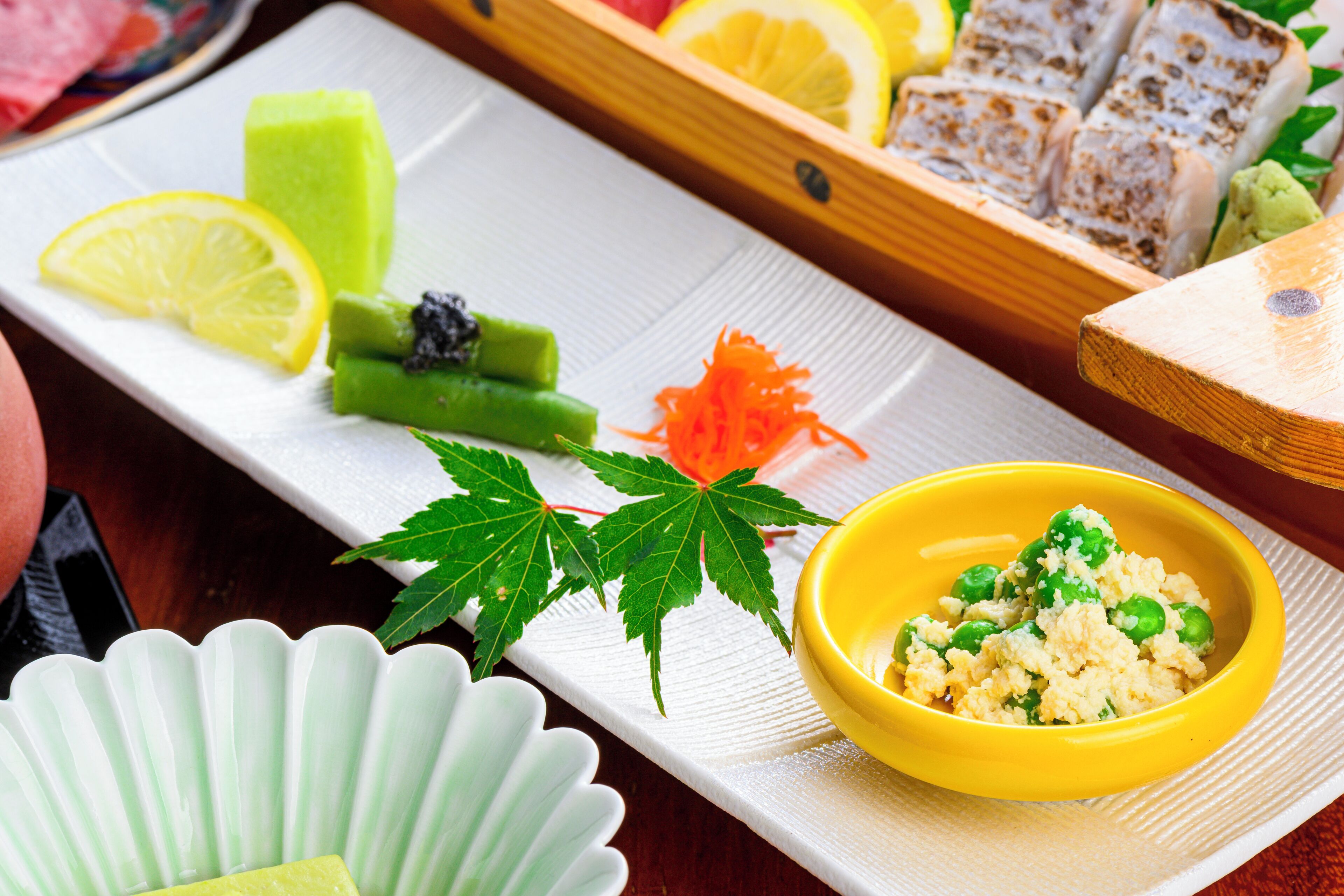 Variedad de alimentos, incluyendo un tazón de arroz con guisantes, rodajas de limón, verduras verdes y una bandeja de madera con comida.