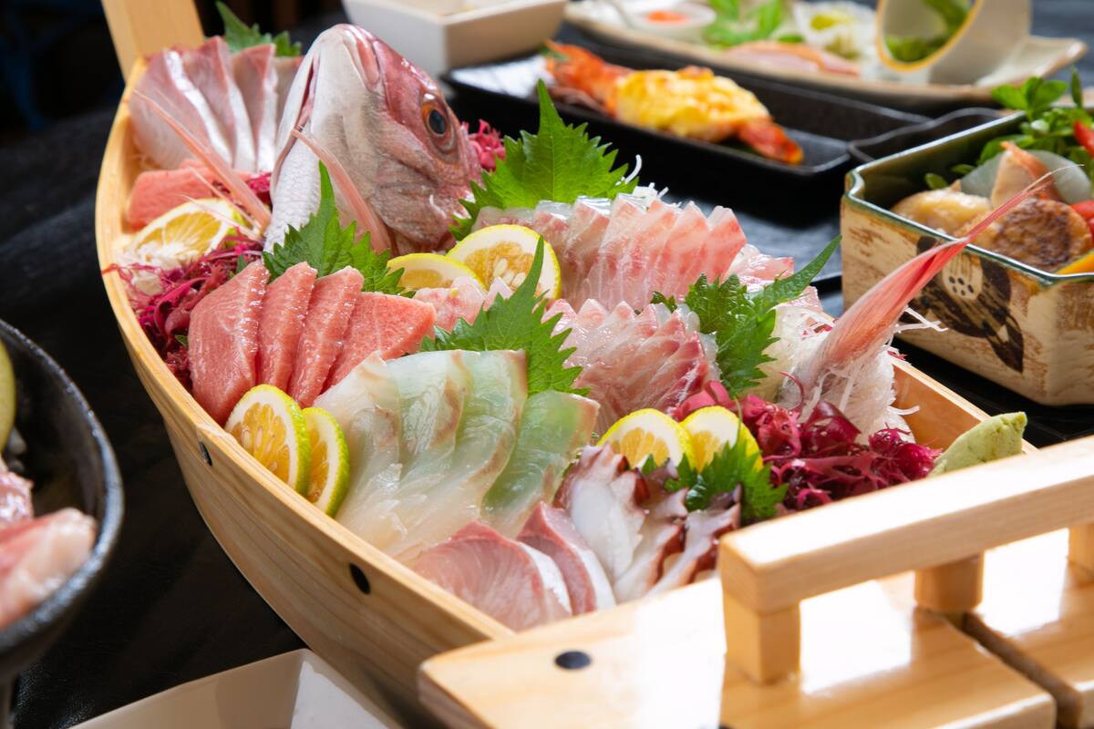 A wooden boat filled with various types of fresh seafood, garnished with lemon slices and green leaves.