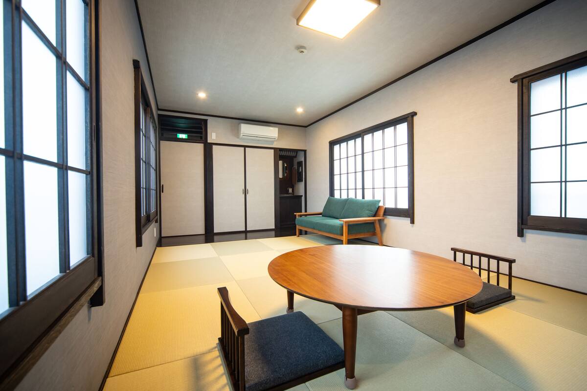A traditional Japanese room with tatami flooring, a tatami mat bench, a low table, and a green cushioned chair.