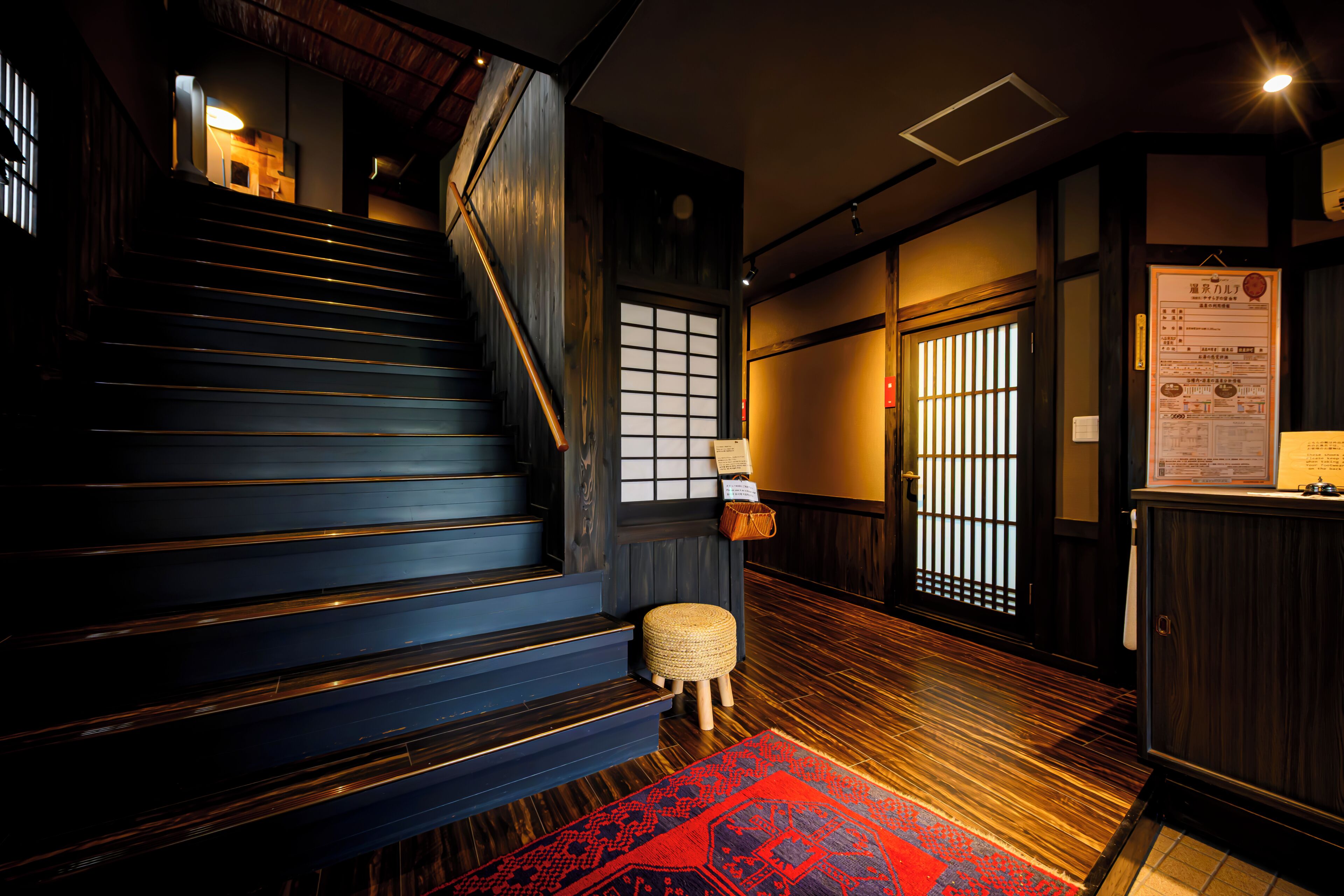 A staircase with wooden steps and a handrail, leading to a room with a traditional Japanese sliding door and a bulletin board with information.