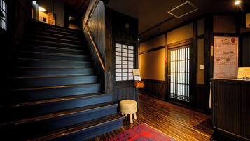 A staircase with wooden steps and a handrail, leading to a room with a traditional Japanese sliding door and a bulletin board with information.