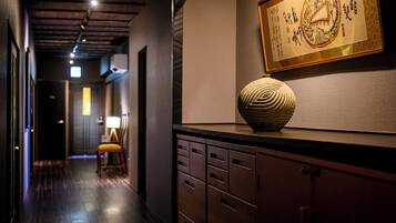 A hallway with a wooden floor, a desk with drawers, a chair, and a framed artwork on the wall.