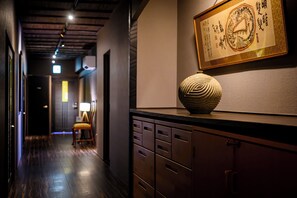 A hallway with a wooden floor, a desk with drawers, a chair, and a framed artwork on the wall.