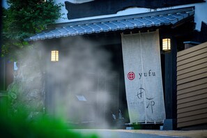 Perinteinen japanilainen rakennus, jossa on tiilikatto, japaninkielisillä merkeillä koristeltu juliste ja kivimuuri.